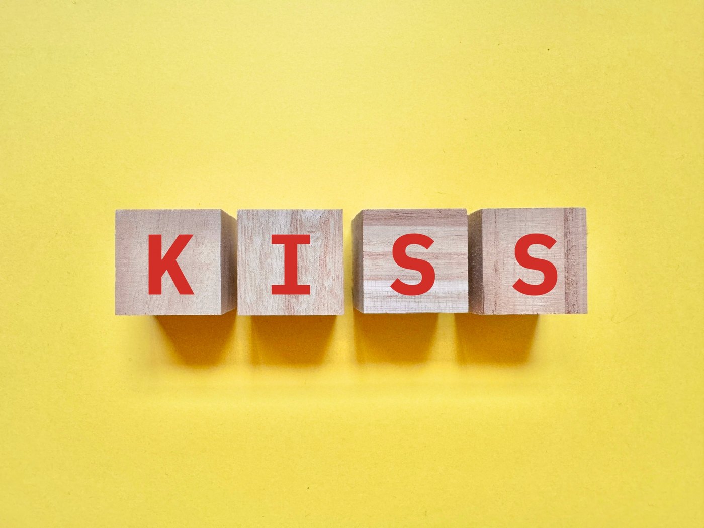 黄色の背景にKISSと並ぶ木製ブロック。キスの種類とフレンチキスを考えるイメージ